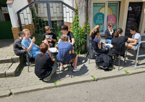 uczniowie siedzą na krzesełkach przed lodziarnią.