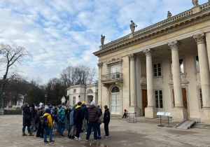 Uczniowie stoją pod pałacem w Łazienkach.