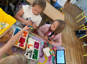 Dziewczynki układają z klocków Lego karuzelę.