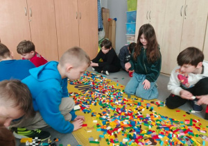 Uczniowie siedzą przy klockach Lego.